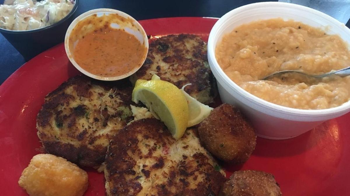 The Crab Cake Dinner at The Shrimp Basket in Gulfport includes three lump crab meat patties served wtih remoulade sayce, shrimp slaw, hush puppies, a corn fritter and an additional side. Here, it’s cheese grits.