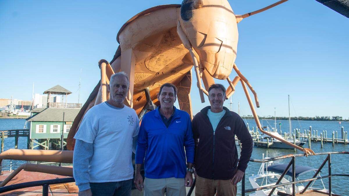 From left, Greg Cenac, Bruno Milanese and Will Ladnier stand in front of a large tugboat with a steel cockroach on top at a pier in Biloxi on Thursday, Nov. 21, 2024. Cenac came up with the idea for the roach sculpture on the tugboat, which will be sunk as a fishing reef and tourist attraction for divers.