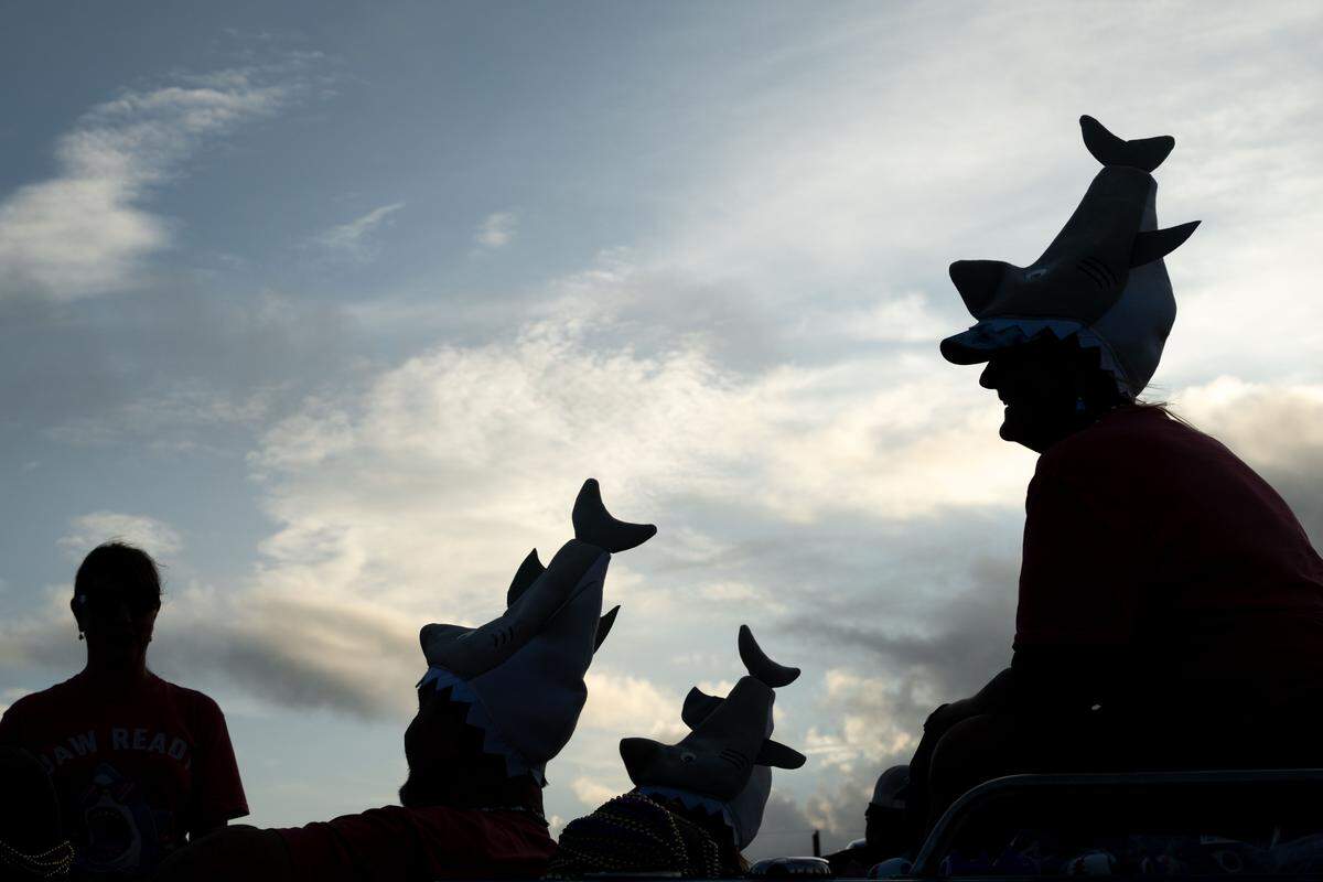 Parade attendees wear shark hats as the sun sets Monday.