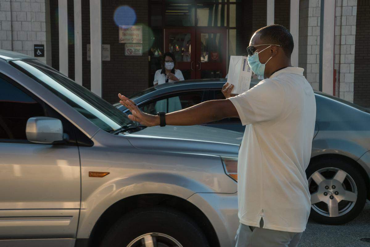 Biloxi High School Driver Ed teacher directs traffic at the student drop off on the first day of school amid the COVID-19 pandemic on August 5th, 2020