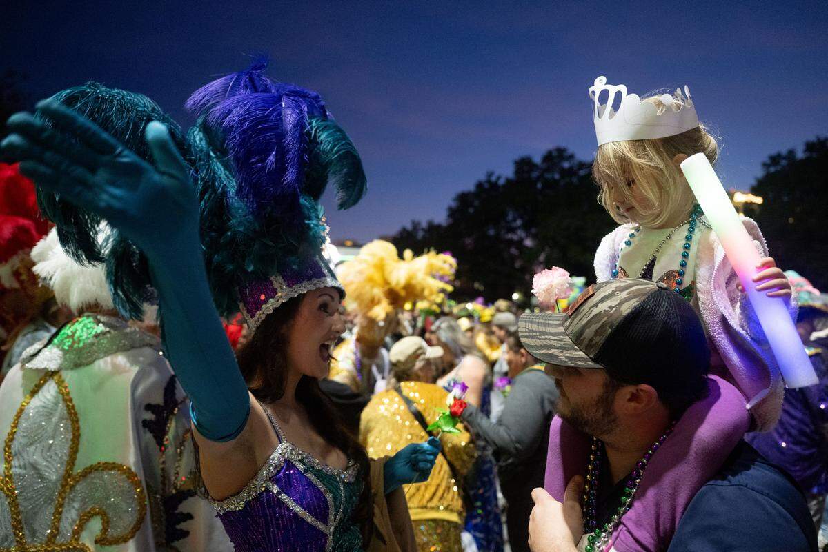 A float attendee waves to a child sitting on her father’s shoulders during a 12th Night Celebration in Biloxi on Monday, Jan. 5, 2026.