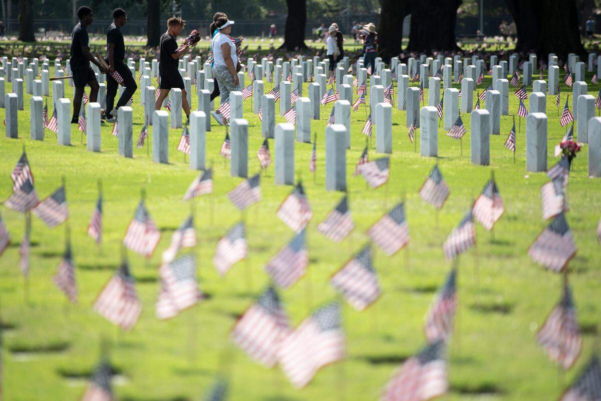 Volunteers help place thousands of tiny American flags on the graves of American service members at Biloxi National Cemetery in Biloxi ahead of Memorial Day on Saturday, May 25, 2024.