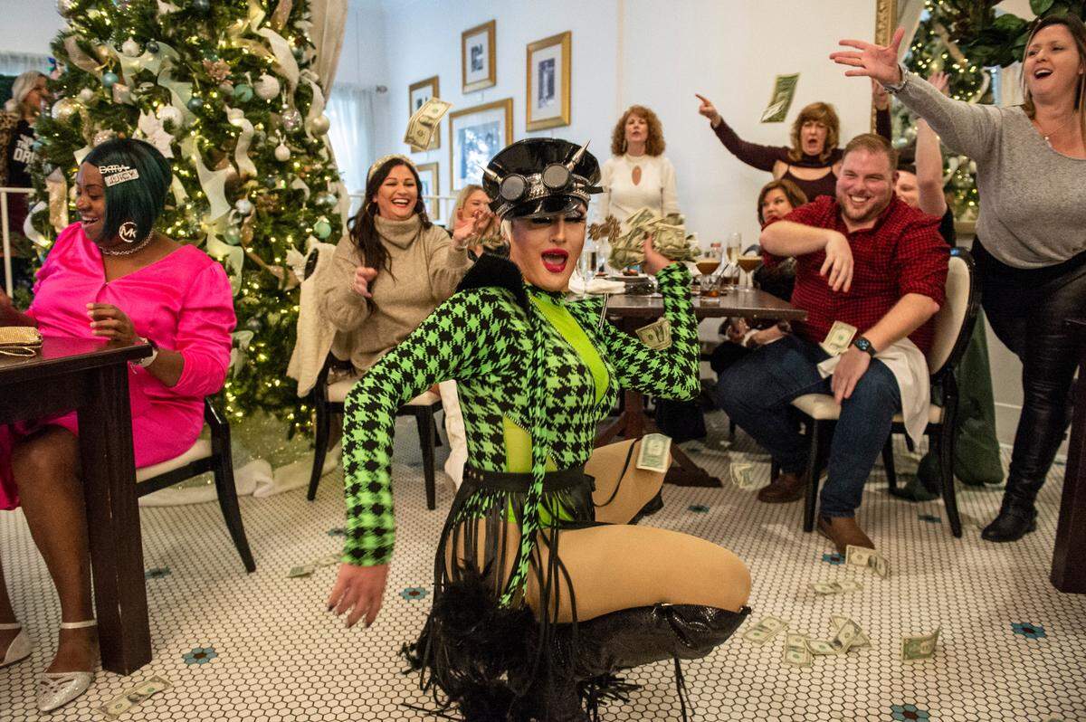 Ivy Dripp drops low in a dance move as brunch guests throw dollar bills at her during drag brunch at White Pillars on Sunday, Dec. 19, 2021. The White Pillars staff supply plenty of dollar bills for guests to exchange their larger bills for.