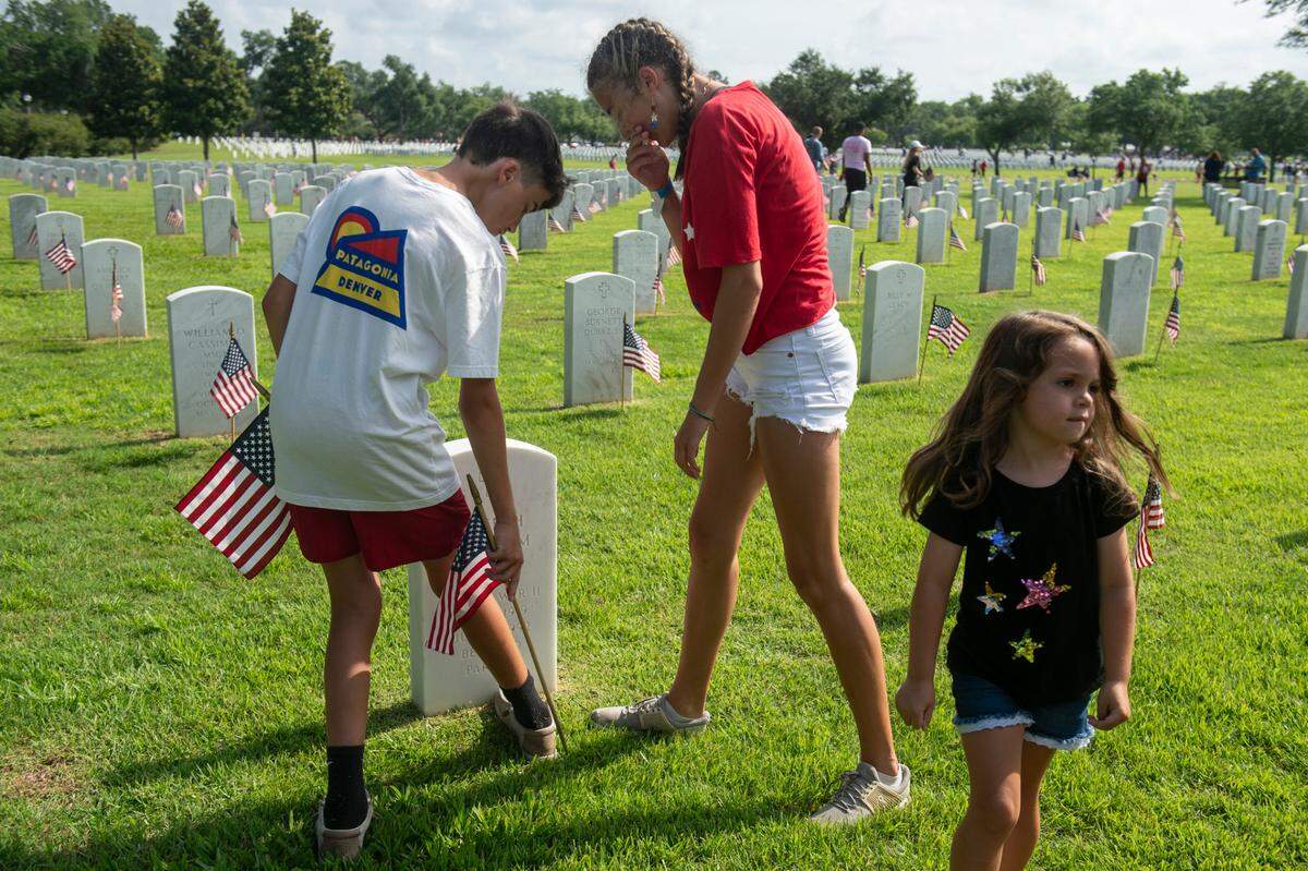 Krislyn Necaise, center, Bryce Necaise and Raegan Henry, right, place a flag on the tombstone of the Necaise’s great grandparents as they help place American flags on the graves of American service members at Biloxi National Cemetery in Biloxi ahead of Memorial Day on Saturday, May 25, 2024.