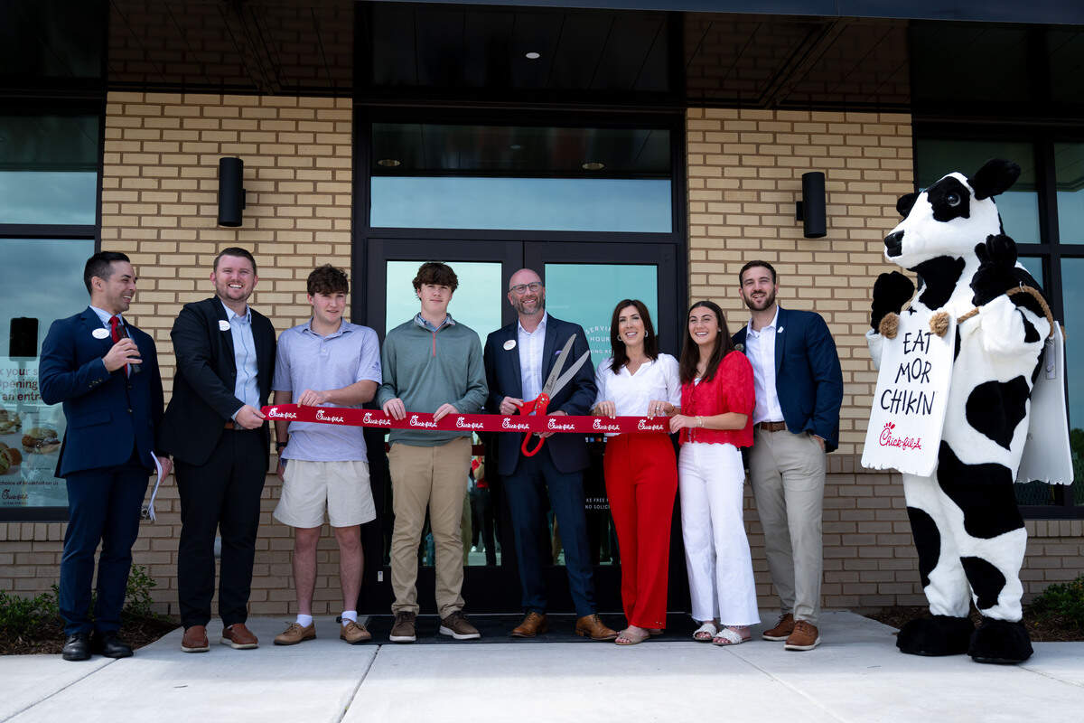 Owner-operator Craig Smith, middle, poses for a photo as he cuts a ceremonial Wednesday at the new Chick-fil-A in Ocean Springs.