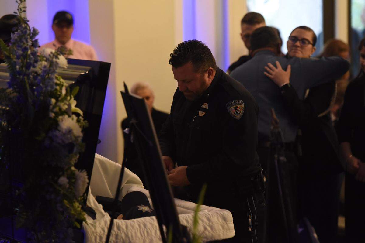 A police officer pays final respects to fallen officers Steven Robin and Branden Estorffe, both killed in the line of duty, at a Bay St. Louis funeral service on Dec. 21, 2022.