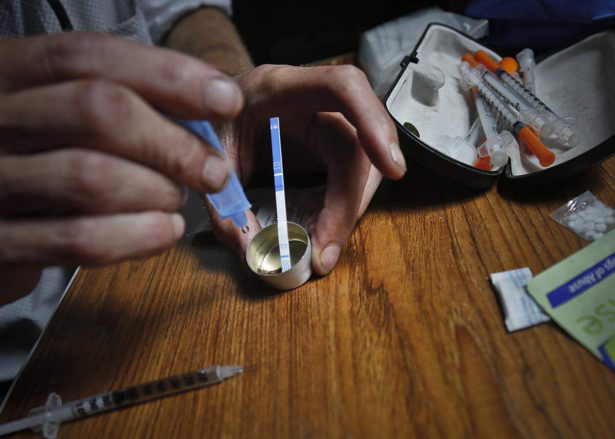 An addict prepares heroin, placing a fentanyl test strip into the mixing container to check for contamination, Wednesday Aug. 22, 2018, in New York. If the strip registers a “pinkish” to red marker then the heroin is positive for contaminants.