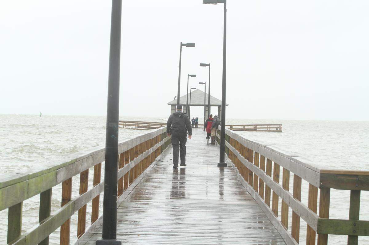 A Biloxi police officer escorts sightseers off the Lighthouse Pier at Porter Avenue, where surge was lapping over the woodwork at had loosened moorings at the pier’s south end.