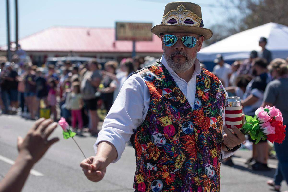 A member of the Ole Biloxi Marching Club hands out a flower during the Jackson County Carnival Association Mardi Gras parade in Pascagoula on Saturday, March 1, 2025.