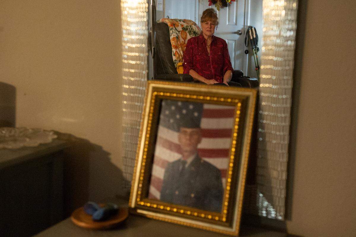 Deborah Tainsh, an author and gold star mother, is reflected in a mirror above a photo of her son Patrick, at her home in Biloxi on Wednesday, Nov. 8, 2023. Patrick died in the war in Iraq.