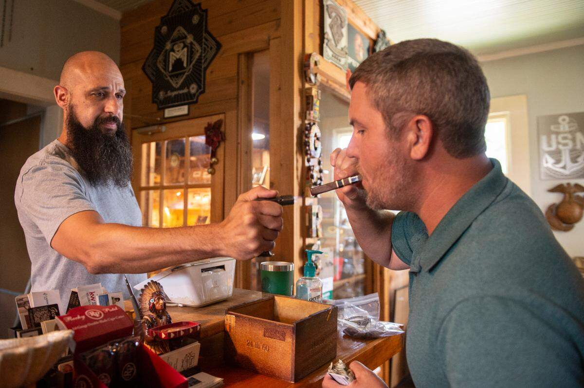 Cigars in the Pass owner Clifton Williams lights a cigar for a customer as he stands behind the register at Cigars in the Pass in Pass Christian on Tuesday, June 27, 2023.