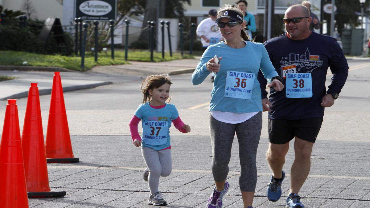 TIM ISBELL/SUN HERALDSophia Martin crosses the finish line with her grandparents, Beth and Steve Martin, in Biloxi on Saturday.