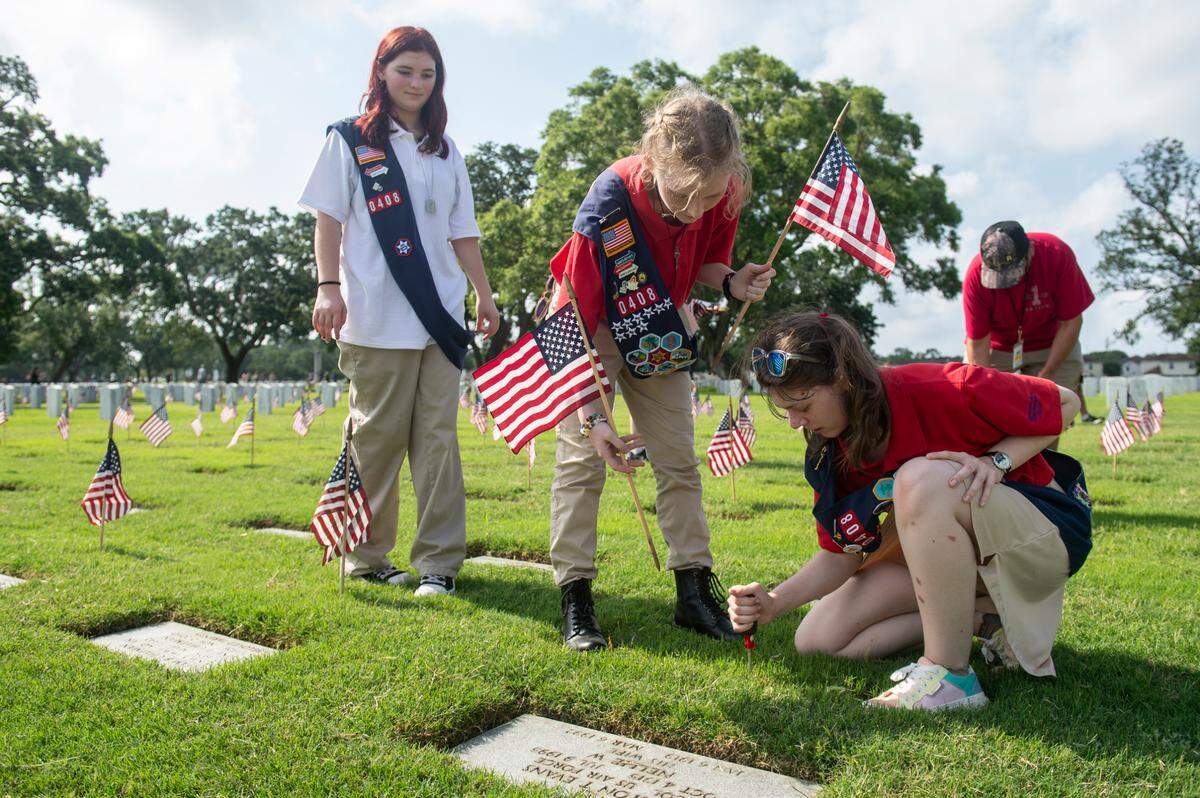 Volunteers from American Heritage Girls troop 0408 help place American flags on the graves of American service members at Biloxi National Cemetery in Biloxi ahead of Memorial Day on Saturday, May 25, 2024.