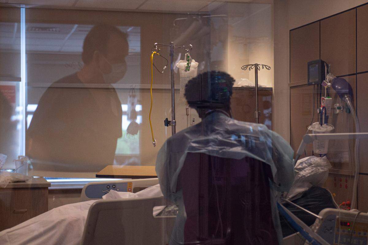 A medical technician cleans a COVID-19 patient’s mouth as a nurses pass by in the ICU at Memorial Hospital in Gulfport on Wednesday, Aug. 11, 2021.