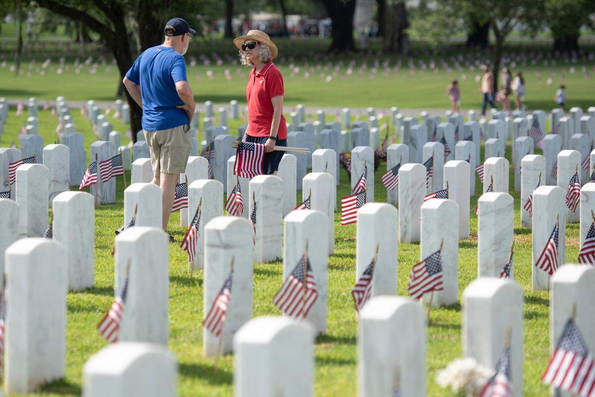 Larry Davis, a retired coast guard member who volunteers to help place the flags most years, and his wife help, decorate the graves of American service members with tiny flags at Biloxi National Cemetery in Biloxi ahead of Memorial Day on Saturday, May 25, 2024.