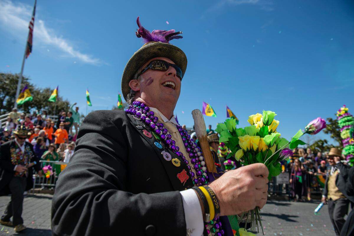 A member of the Ole Biloxi Marching Club passes out plastic flowers during the Gulf Coast Carnival Association Mardi Gras Parade in Biloxi on Tuesday, March 1, 2022.