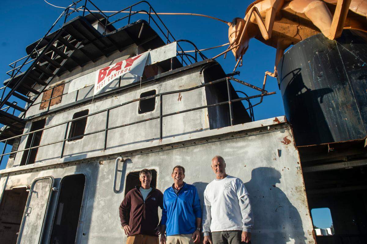 From left, Will Ladnier, Bruno Milanese and Greg Cenac stand in front of an old tugboat with a steel cockroach on top at a pier in Biloxi on Thursday, Nov. 21, 2024. The boat will be sunk as an artificial reef, sponsored by Milanese’s company, Bay Pest Control.