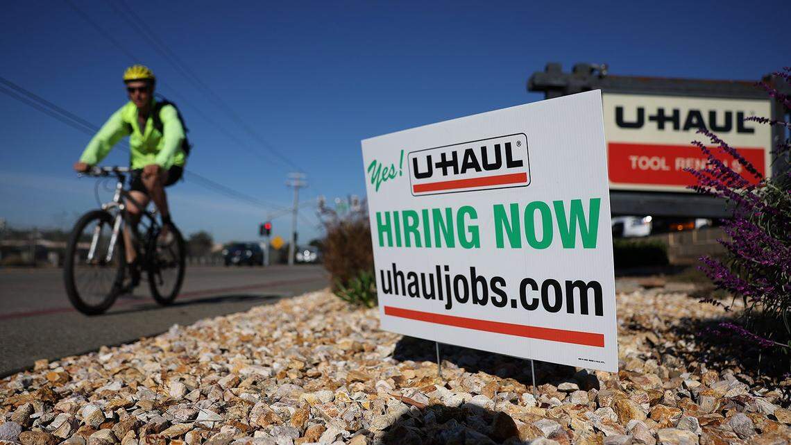 A cyclist rides by a now hiring sign posted in front of a U-Haul rental center earlier this year.