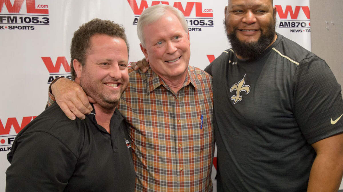 Jim Henderson, the legendary New Orleans Saints play-by-play announcer for the past 30 years, is hugged by Kristian Garic, left, a WWL sportscaster, and Deuce McAllister, a former Saints running back and a current WWL sportscaster, after Henderson announced his retirement at the WWL radio studios in New Orleans, La. Thursday, Feb. 1, 2018.