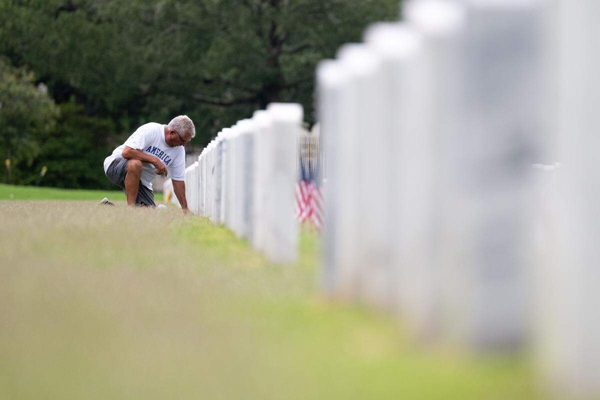 Brian Nunez kneels at a tombstone for his parents during a ceremony at Biloxi National Cemetery on Monday, May 25, 2026.