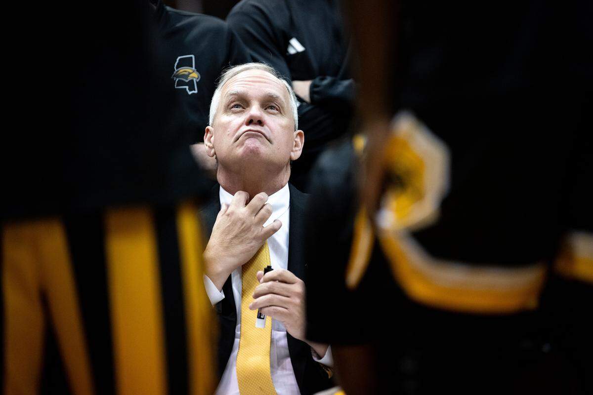 Southern Mississippi head coach Jay Ladner adjusts his tie while in a huddle with his players during a basketball game at The Coliseum on Saturday, Dec. 13, 2025.  Ole Miss won the game 71-67.