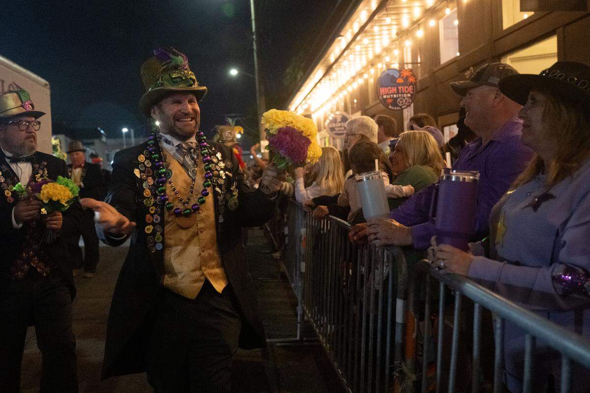 Parade participants pass out flowers to attendees during the Krewe of Neptune parade in Biloxi on Saturday, Feb. 14, 2026.
