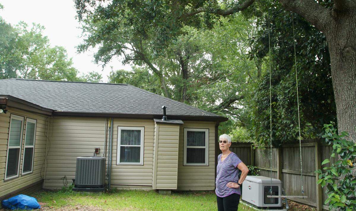 Biloxi homeowner Lynda Keefe stands under a Live oak that her insurance company recommended she trim or remove, saying it could damage her house during a storm.