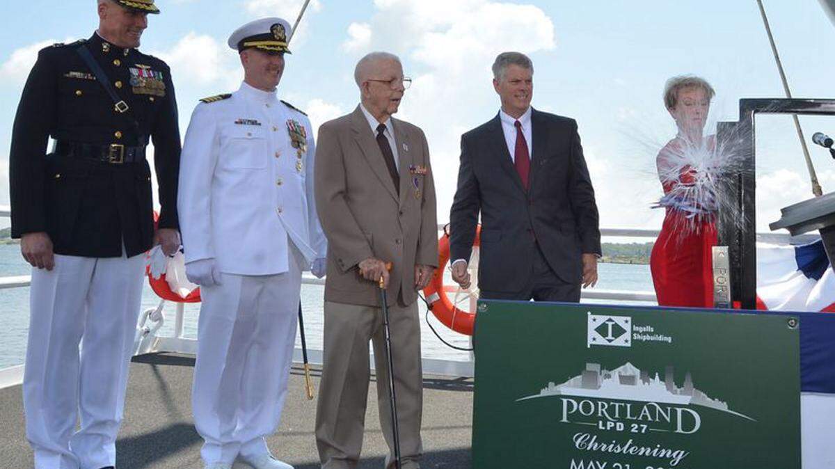 LANCE DAVIS/HII 
 Ship Sponsor Bonnie Amos christens the amphibious transport dock Portland, accompanied by U.S. Marine Corps Maj. Gen. Christopher Owens, left, director of the U.S. Navy's expeditionary warfare division; Capt. Jeremy Hill, Portland's prospective commanding officer; Ted Waller, a World War II veteran who served on the first USS Portland; and Brian Cuccias, Ingalls Shipbuilding president.