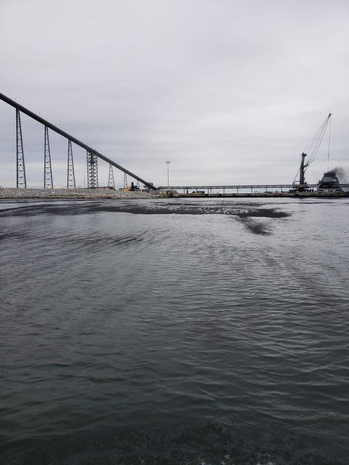 The dust is visible on the surface of the water in this photo, and can be seen blowing in the air from the loading equipment.