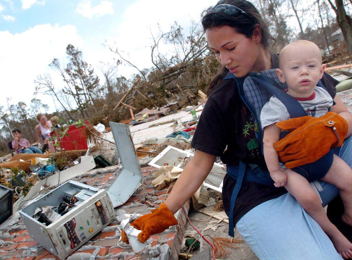 Stephanie Carroll, of Kosciusko, helps search for salvageable items at her parents' home, while holding her ninth-month-old son, Mark, in Diamondhead, on Tuesday, September 6, 2005. Her parents stayed at her home during the storm.