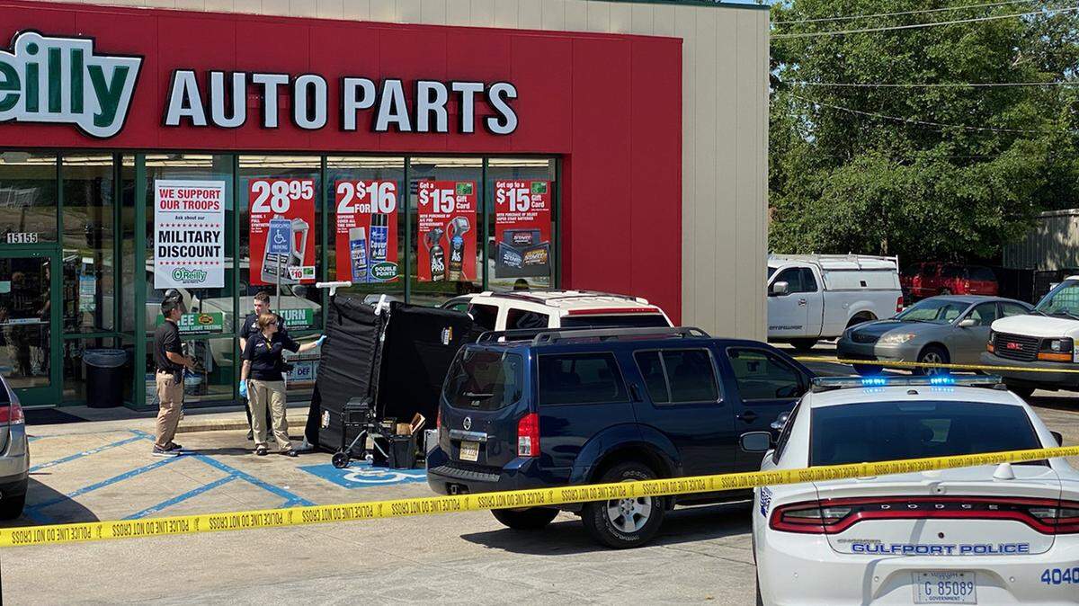 Law enforcement officials stand near a black cover shielding the body of a man shot and killed in front of the O’Reilly Auto Parts atore on Dedeaux Road in Gulfport on Monday, June 14, 2021.