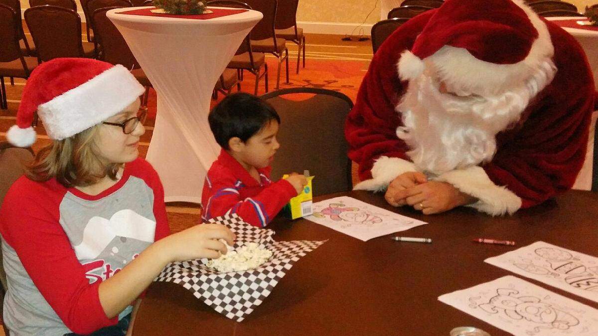 VETO ROLEY/SPECIAL TO THE SUN HERALD 
 Reese Roberts, left, looks on as Santa colors with Adrian Zei during the Pascagoula Hilton Garden Inn's Gifts of Giving party Wednesday, Dec. 16, 2015.