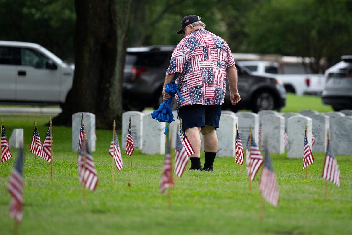 An event attendee walks through a field with American flags during a ceremony at Biloxi National Cemetery on Monday, May 25, 2026.