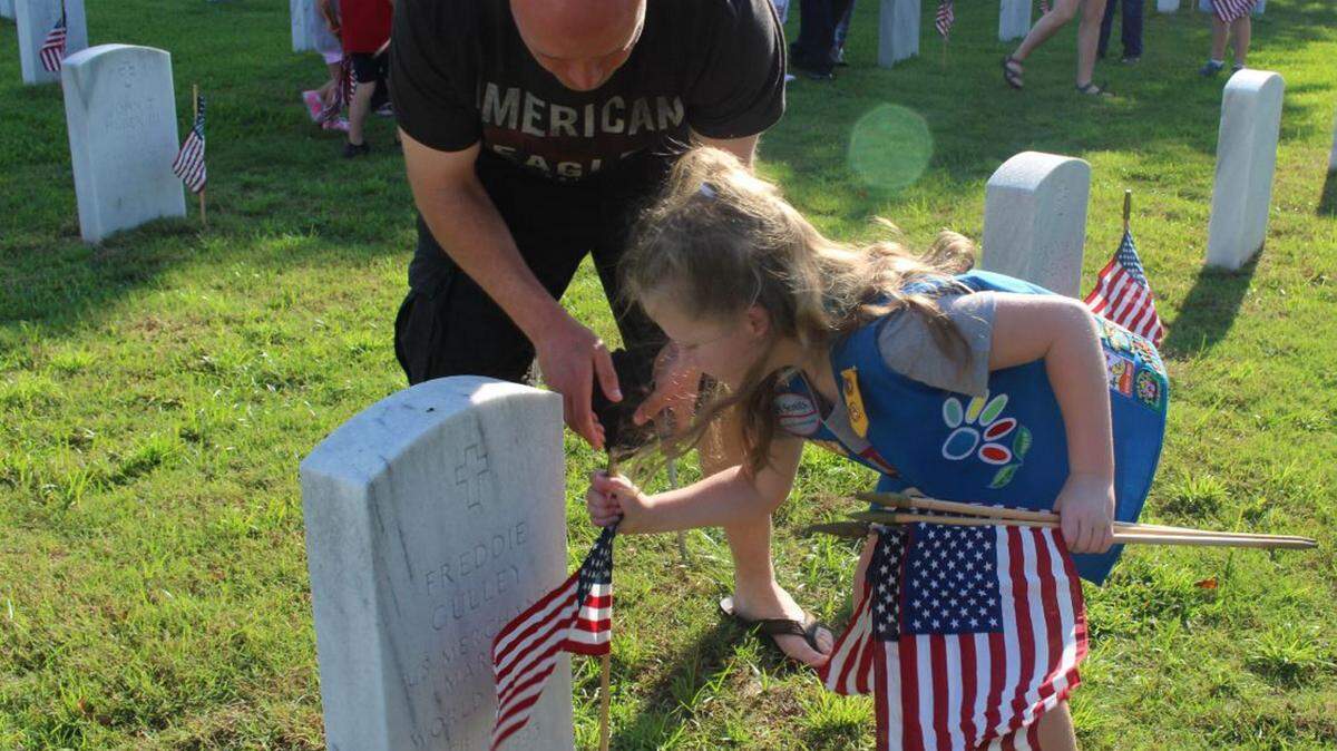 JEFF CLARK/SUN HERALD 
 Daisy Scout Makalyla Foster carefully places a flag near a grave marker at Biloxi National Cemetery while her father, Josh Foster, looks on Saturday, May 28, 2016, in observance of Memorial Day.