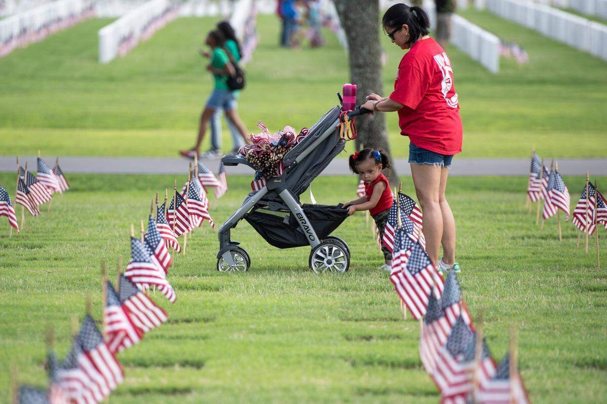 Volunteers help place thousands of tiny American flags on the graves of American service members at Biloxi National Cemetery in Biloxi ahead of Memorial Day on Saturday, May 25, 2024.