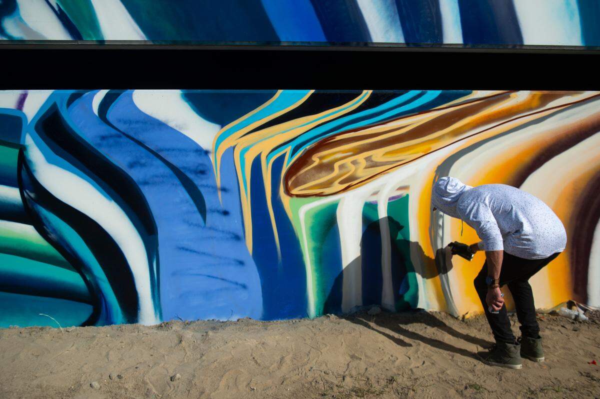 Niko Cook, a local Ocean Springs artist, helps install a mural by Douglas Hoekzema, also known as Hoxxoh, on a parking garage at the new OS 1515 development in downtown Ocean Springs on Tuesday, Oct. 29, 2024.
