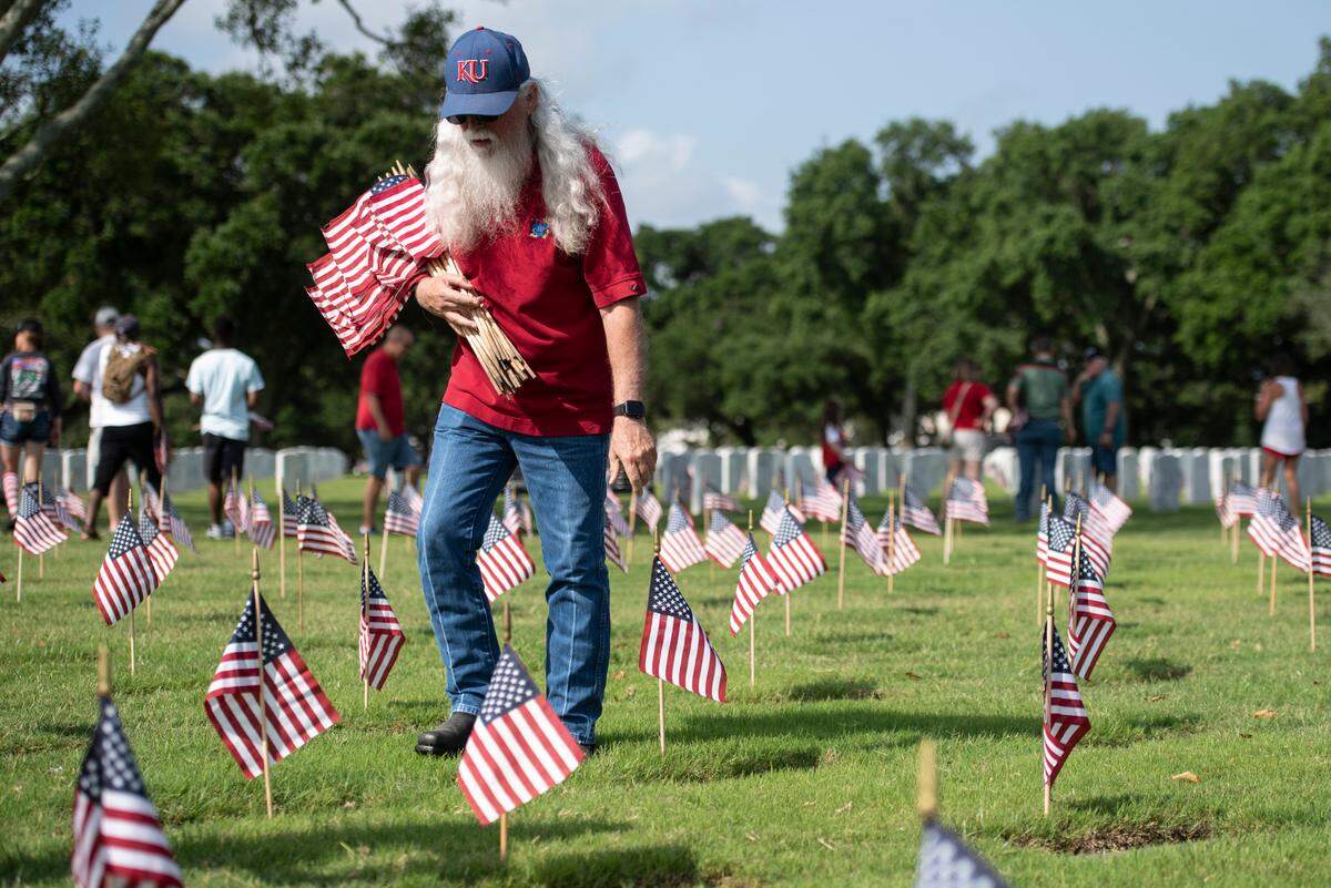 Volunteers help place thousands of tiny American flags on the graves of American service members at Biloxi National Cemetery in Biloxi ahead of Memorial Day on Saturday, May 25, 2024.