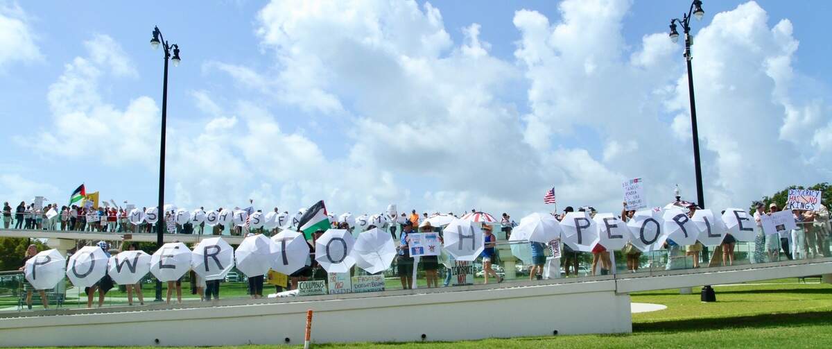 After speeches Saturday in downtown Gulfport at the “No Kings” protest, volunteers carrying umbrellas led a crowd across an elevated walkway, where they displayed the words “Power to People” and “MS fights fascism” for passing motorists on the beach highway at Jones Park.