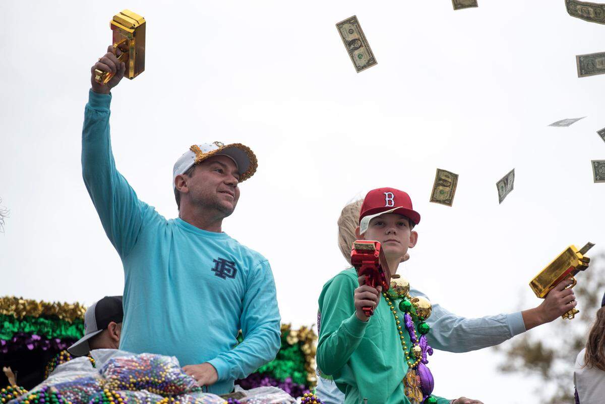Float riders use money guns to throw dollar bills to the crowd during the Gulf Coast Carnival Association Mardi Gras parade in Biloxi on Tuesday, March 4, 2025.