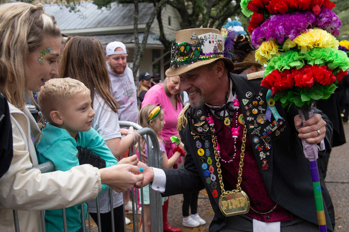 A member of the Ole Biloxi Marching Club hands out plastic roses during The Ocean Springs Elks Carnival Parade in downtown Ocean Springs on Saturday, Jan. 27, 2024.
