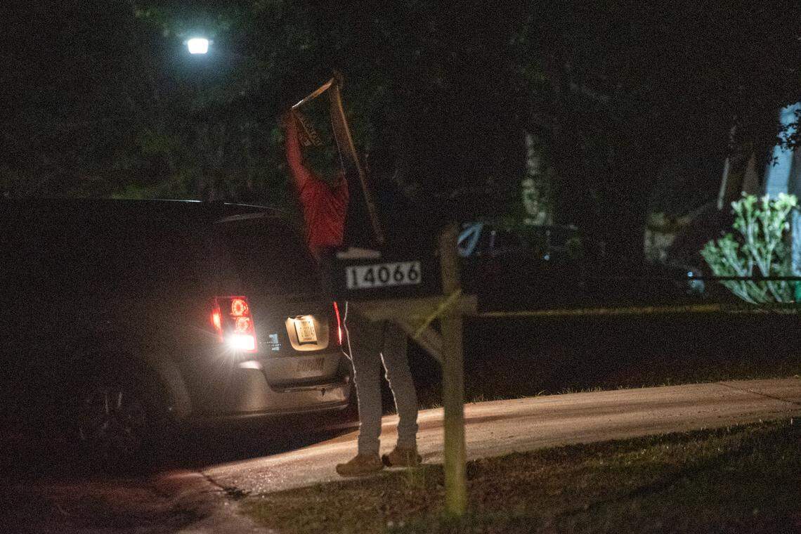 Police officers lift up crime scene tape to allow the coroner to back into a driveway on Oakview Circle in Latimer on Thursday, April 7, 2022.
