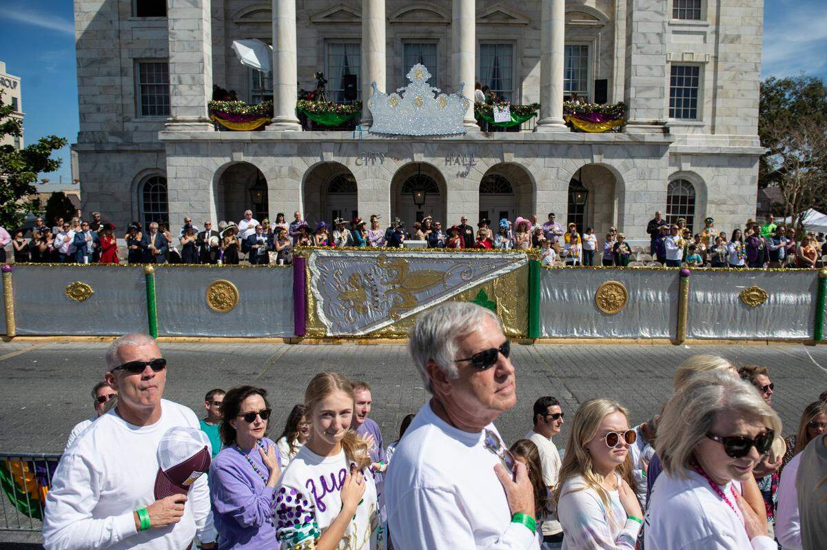 Parade attendees stand at attention for the national anthem before the Gulf Coast Carnival Association Mardi Gras Parade in Biloxi on Tuesday, March 1, 2022.