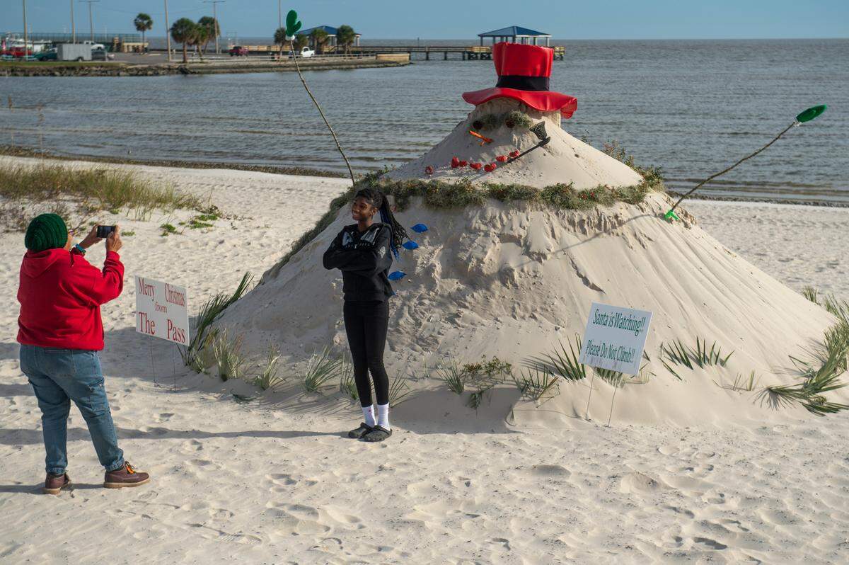 Visitors pose in front of Pass Christian’s “Sandyman”, which is a snowman made out of sand, on Pass Christian Beach on Thursday, Nov. 30, 2023.