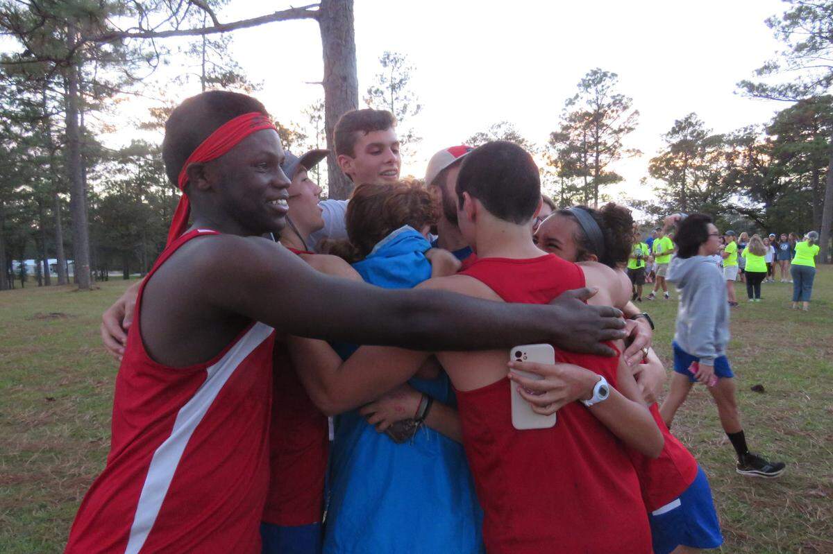 Andre Briggs, far left, joins a group hug after the regional cross country meet on Oct. 26, 2021.