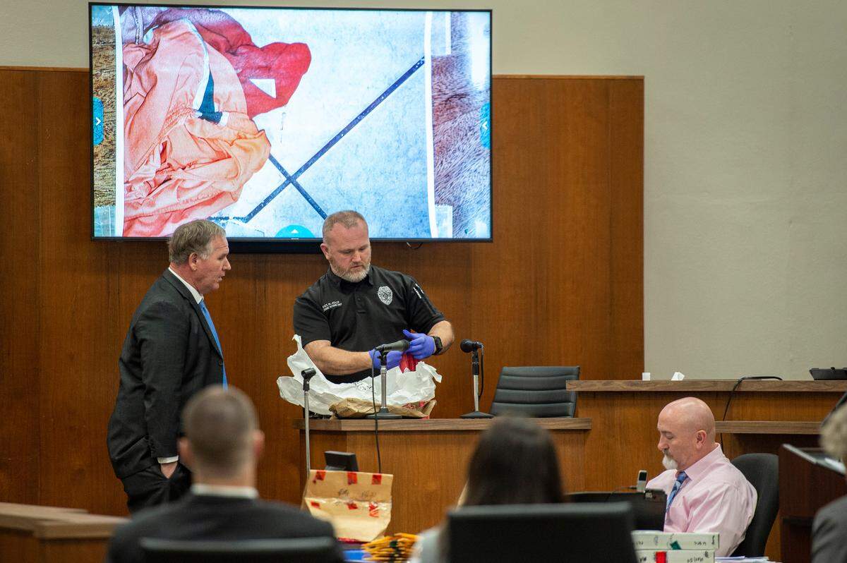 Sgt. Robert Jolly, center, examines a piece of evidence and compares it to a photograph taken at the scene of the murder of Penny Clark while he is on the witness stand during trial at Harrison County Circuit Court in Biloxi on Tuesday, March 8, 2022.