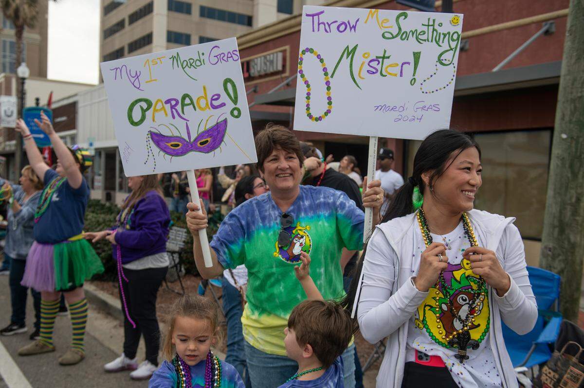 Paradegoers hold signs during the Krewe of Gemini parade in downtown Gulfport on Saturday, Feb. 10, 2024.