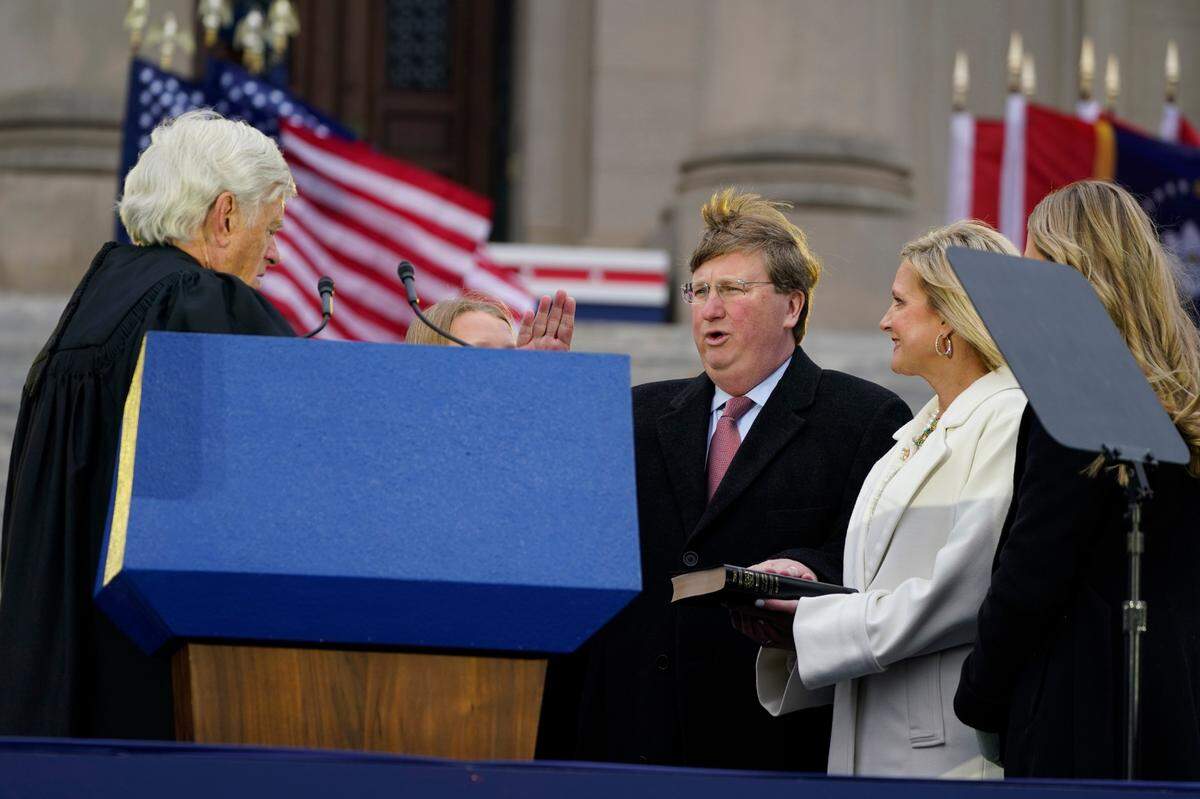 A strong wind blows across the Mississippi State Capitol grounds Tuesday as Gov. Tate Reeves, center, recites the oath of office as given to him by Mississippi Supreme Court Chief Justice Michael Randolph, left, while his wife Elee Reeves, right, holds the family Bible during the inauguration ceremony in Jackson.