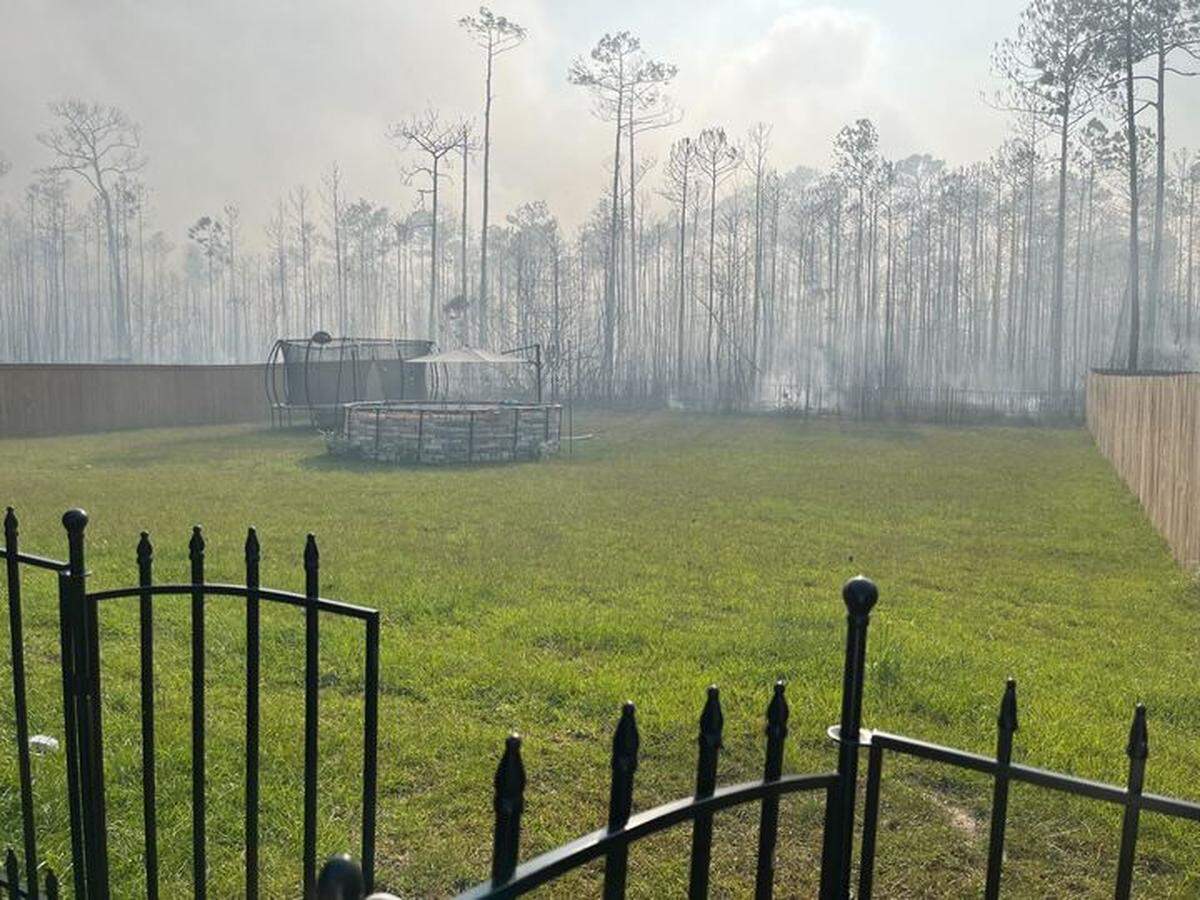 Smoke is visible in a backyard while a fire burns near the Talla Pointe subdivision in Jackson County.