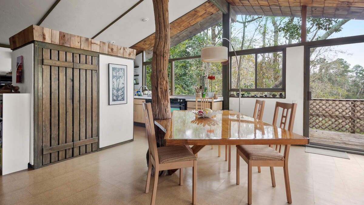 Designer and builder Carroll Ishee’s unique style is on display in this house for sale on Brumbaugh Road in Ocean Springs, which he built for his daughter. An Ishee cabinet, left, serves as a partition between the kitchen and open dining and living area. A second signature feature can be seen in the tree trunk incorporated into the house design and table, along with the large windows that allow natural light to pour in.