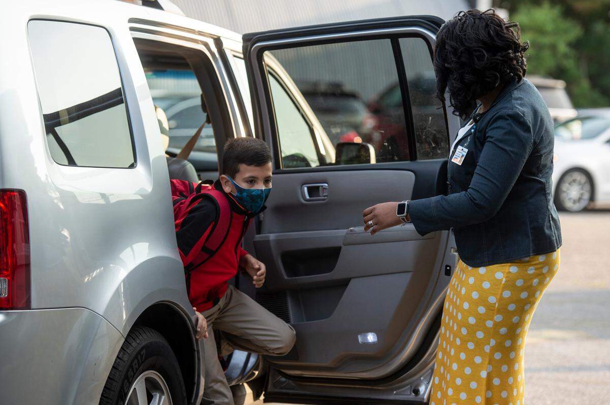 Assistant Principal Stacy Williams opens a car door for third grader Jandiel Garcia Rodriguez as his parents drop him off on the first day of the school year at Gautier Elementary.
